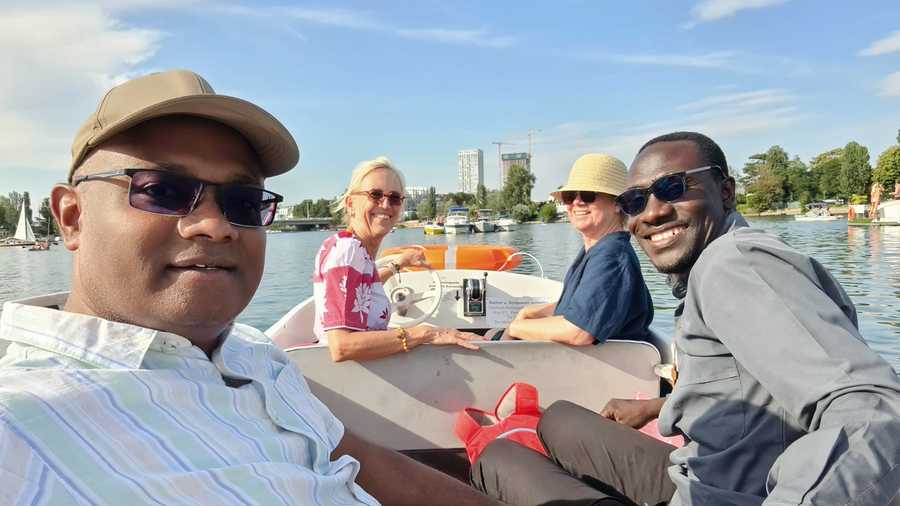 Vier Personen, darunter ein Mann mit Sonnenbrille, sitzen in einem Boot auf dem Wasser. Sie alle lächeln und genießen ihre Zeit miteinander